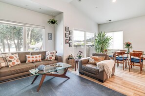 A spacious living room with a brown leather sofa, a glass coffee table, and a dining area with wooden chairs and a table. - Half Moon Bay Vacation Rental: 1 Mile to Beach! (Half Moon Bay)