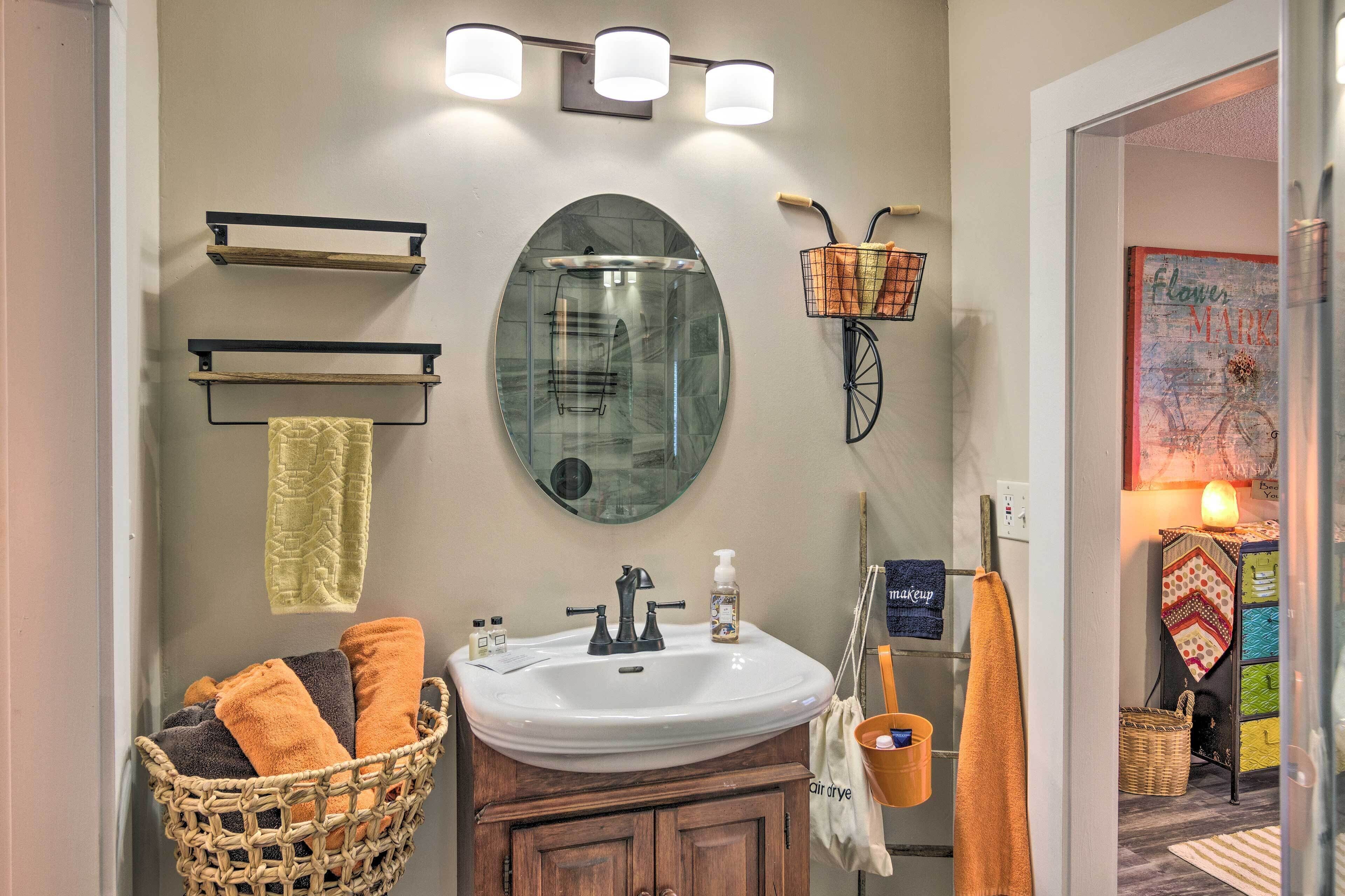 A bathroom with a white sink, wooden cabinets, a round mirror, and a wicker basket.