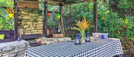 A covered outdoor seating area with a checkered tablecloth, stone walls, hanging planters, and lanterns.