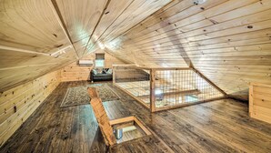 A high-ceilinged attic room with wooden floors and walls, a small window, and a bed. - Peaceful Decatur Cabin w/ Grill & Fire Pit! (Decatur)