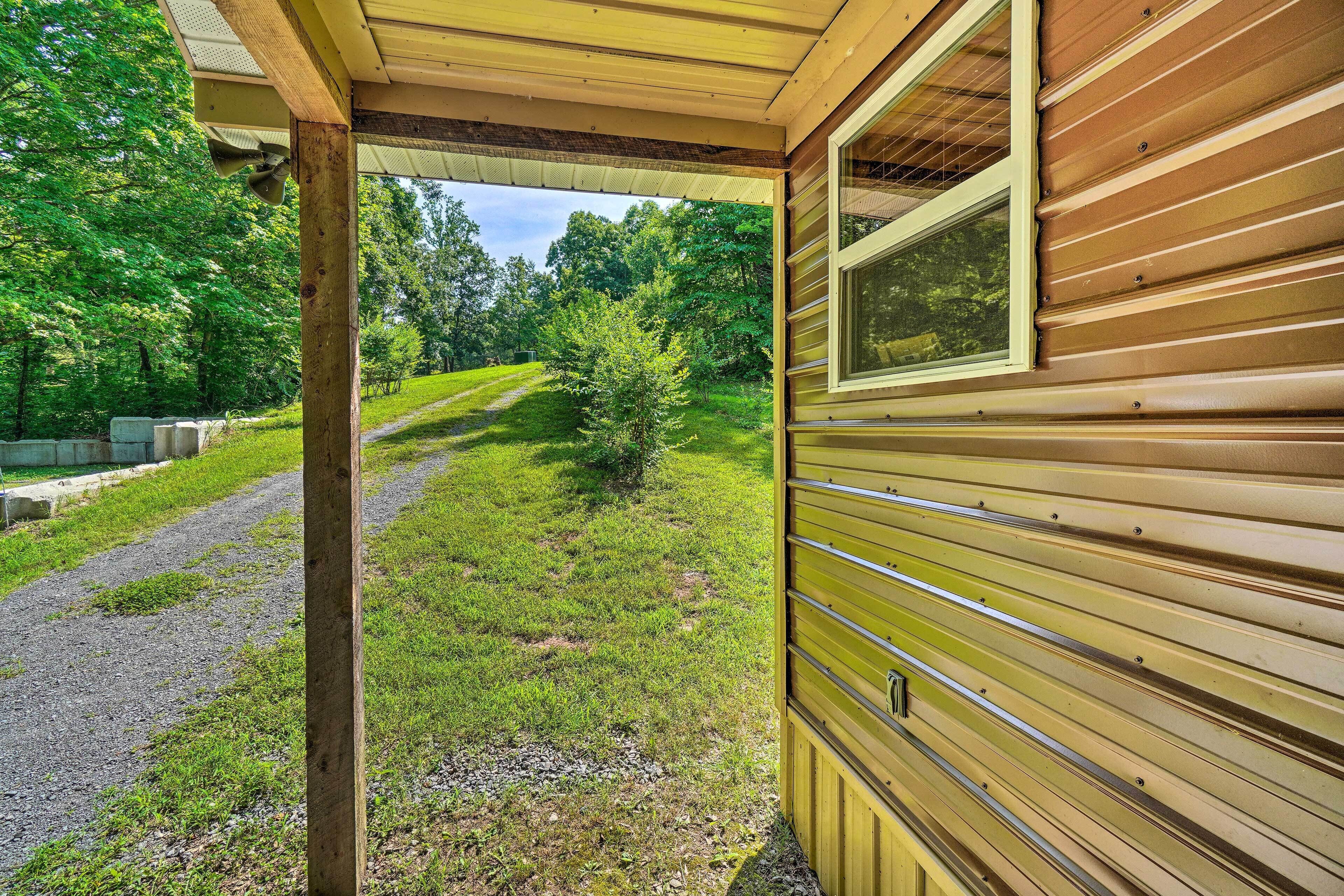 A wooden cabin with a covered porch, a gravel path, and a view of a forested area.
