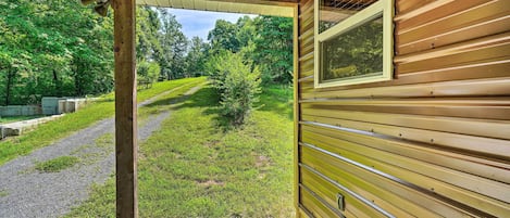 A wooden cabin with a covered porch, a gravel path, and a view of a forested area.