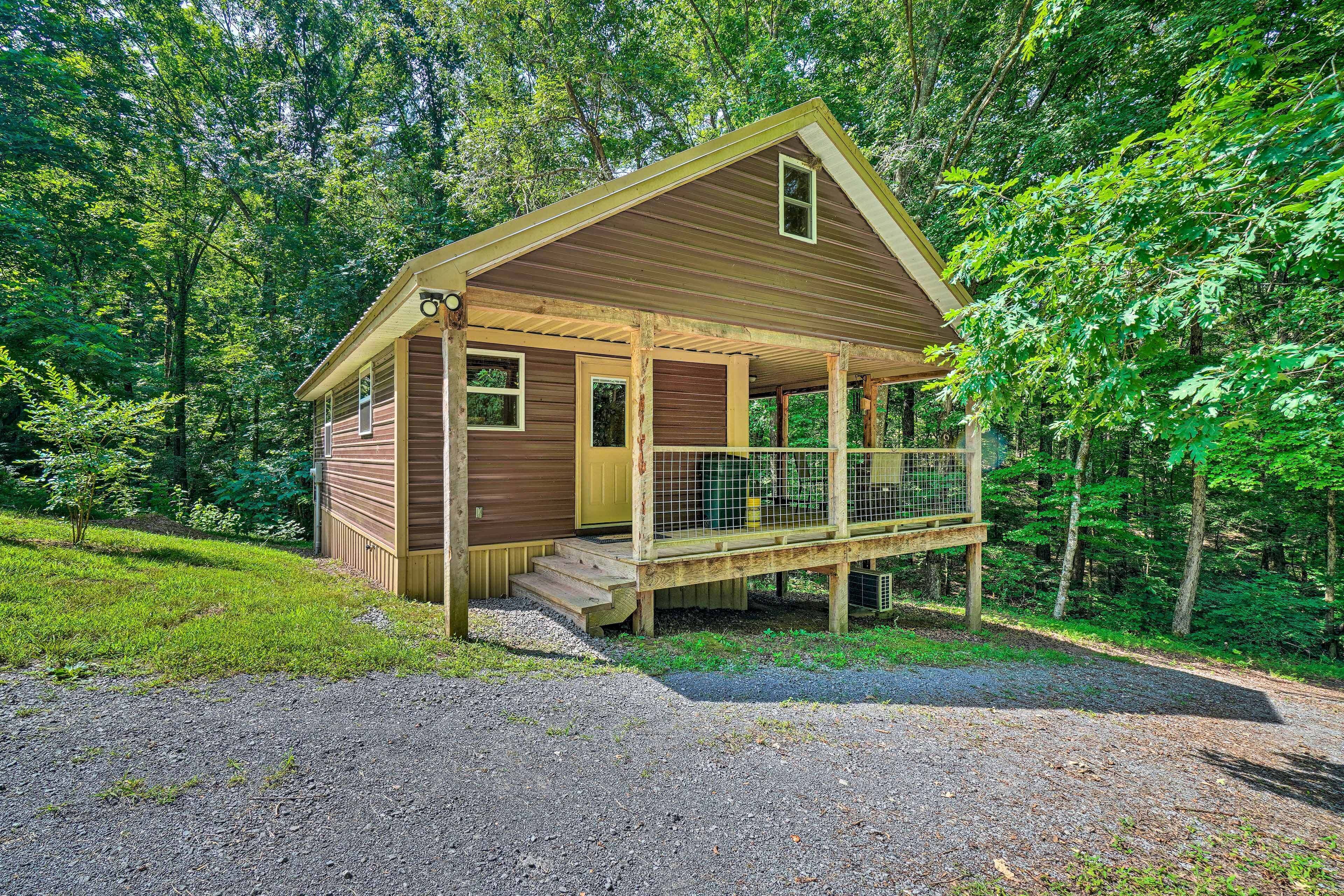 A wooden cabin with a porch, surrounded by trees.