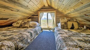 A cozy attic bedroom with two beds, a window with curtains, and a view of the outdoors. - Pano Views! Custom Cabin on Rocky Mountain Front (Augusta)