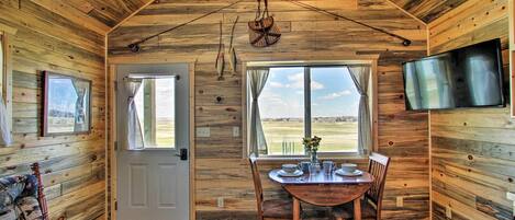 A wooden cabin interior with a dining area, a TV mounted on the wall, and a door leading outside.