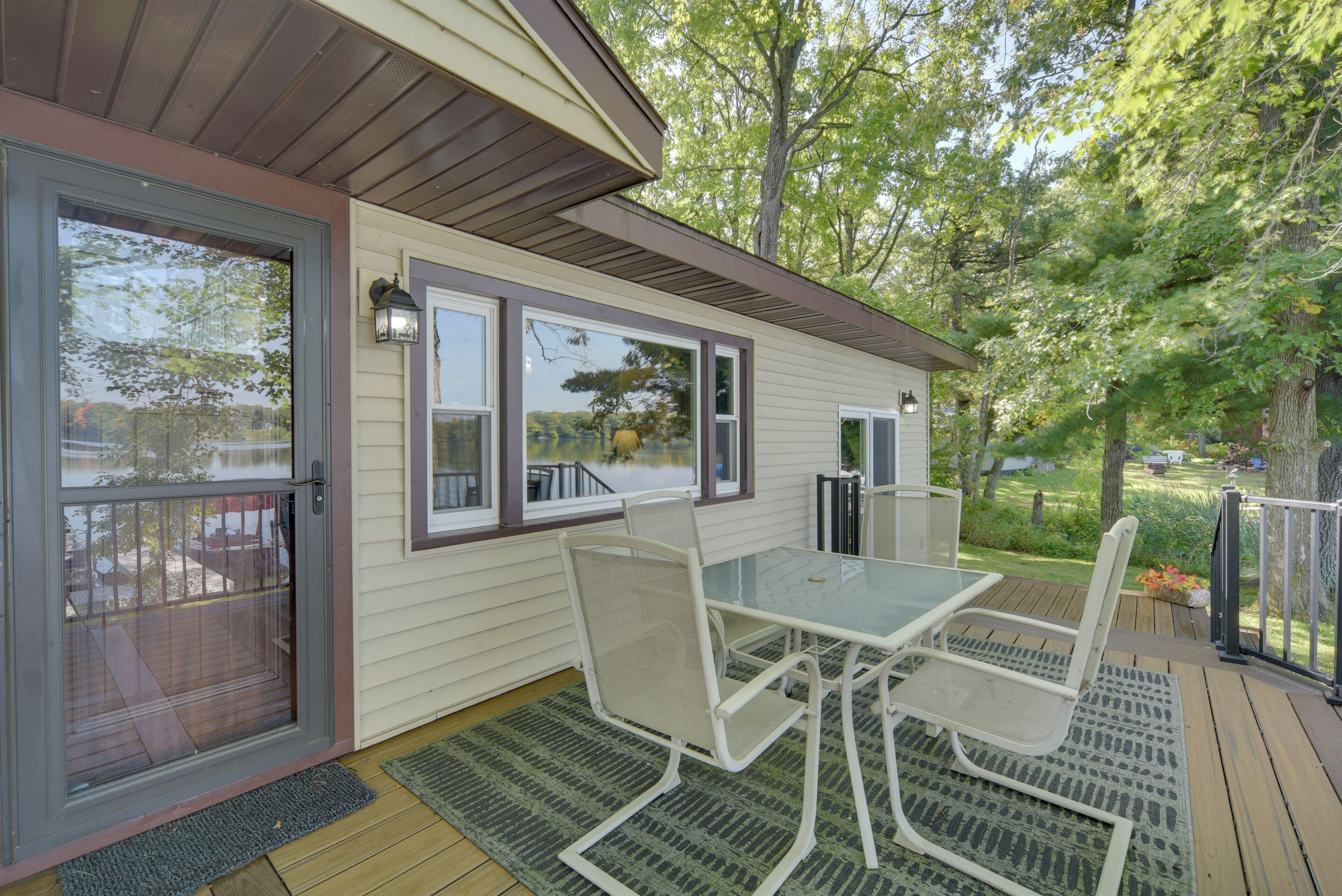 A covered patio with a glass table and chairs, a door with a screen, and a view of a lake and trees.