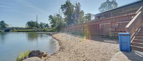 A riverside walkway with a wooden fence, a blue trash bin, and a building with a sloped roof.