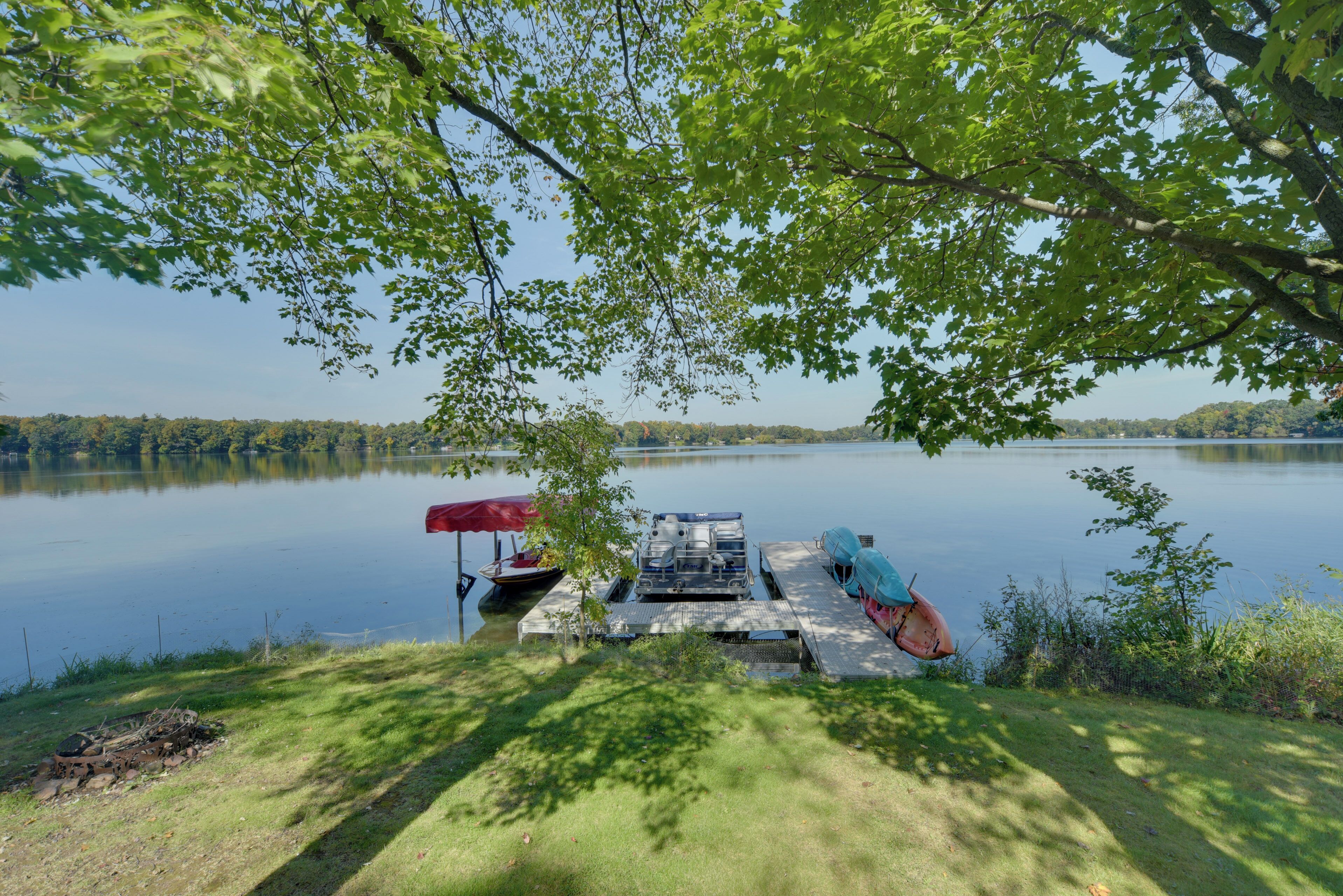 A dock with boats and a red umbrella by a calm lake surrounded by trees.