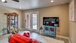 A spacious living room with a ceiling fan, a large flat-screen TV, a red sofa, and a decorative mirror. - Walk to Texas Tech! Cozy Lubbock Gem w/ Patio (Lubbock)