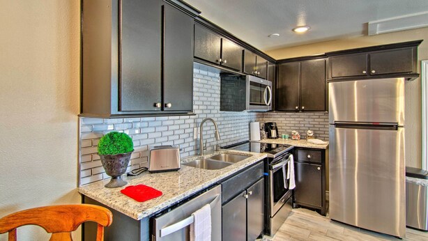 A modern kitchen with dark cabinets, stainless steel appliances, and a granite countertop. - Walk to Texas Tech! Cozy Lubbock Gem w/ Patio (Lubbock)