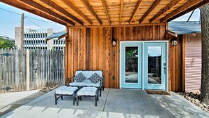 A covered patio area with a wooden ceiling, a bench with cushions, and a door with a glass panel. - Walk to Texas Tech! Cozy Lubbock Gem w/ Patio (Lubbock)