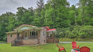 A two-story house with a brick exterior, a red roof, and a porch with red Adirondack chairs.