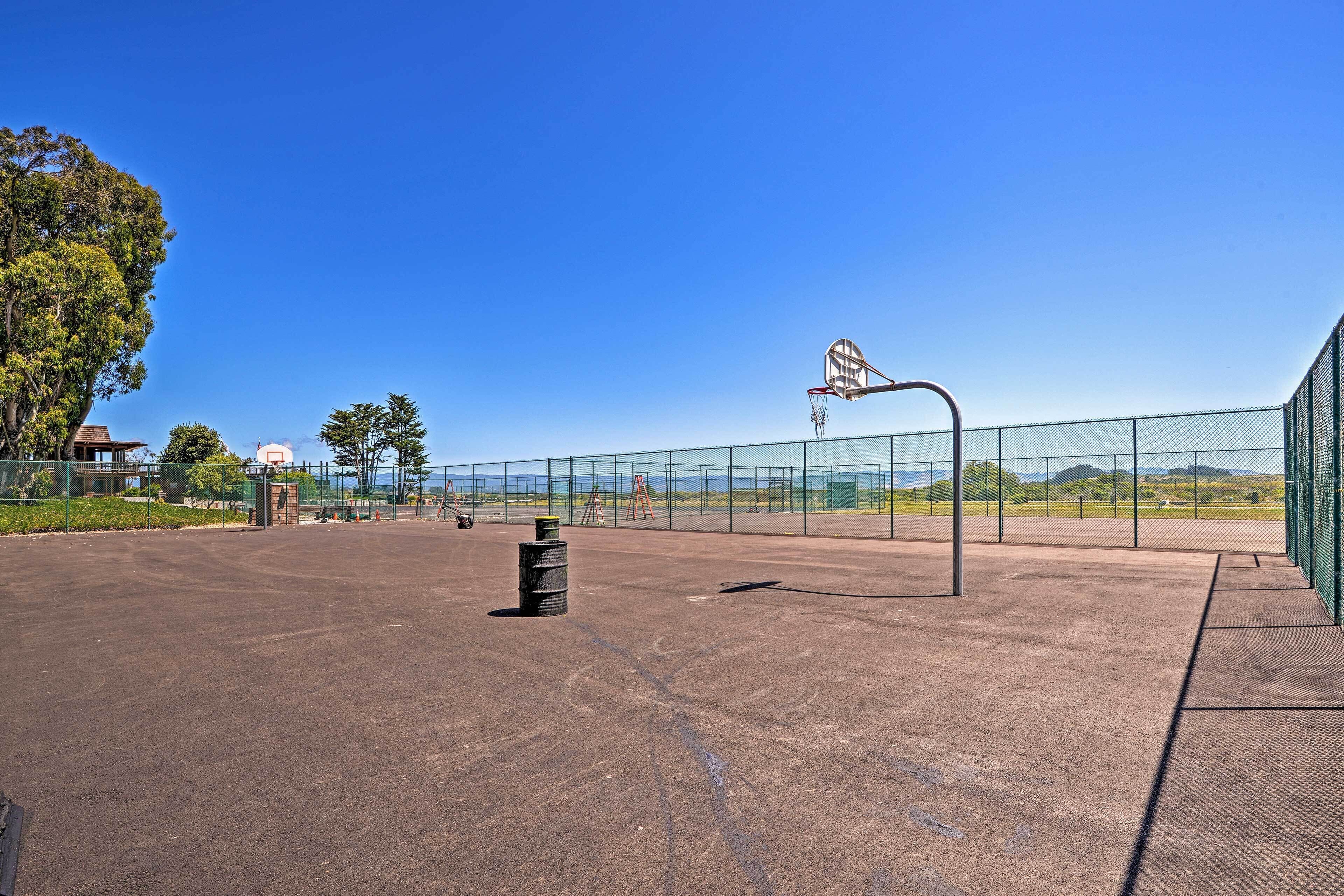 Una cancha de baloncesto al aire libre con una red, un bote de basura y una valla.