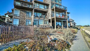 A multi-story building with balconies and large windows, situated near a sandy area with a wooden walkway. - Beachfront Pajaro Dunes Condo w/ Bay Views! (Watsonville)