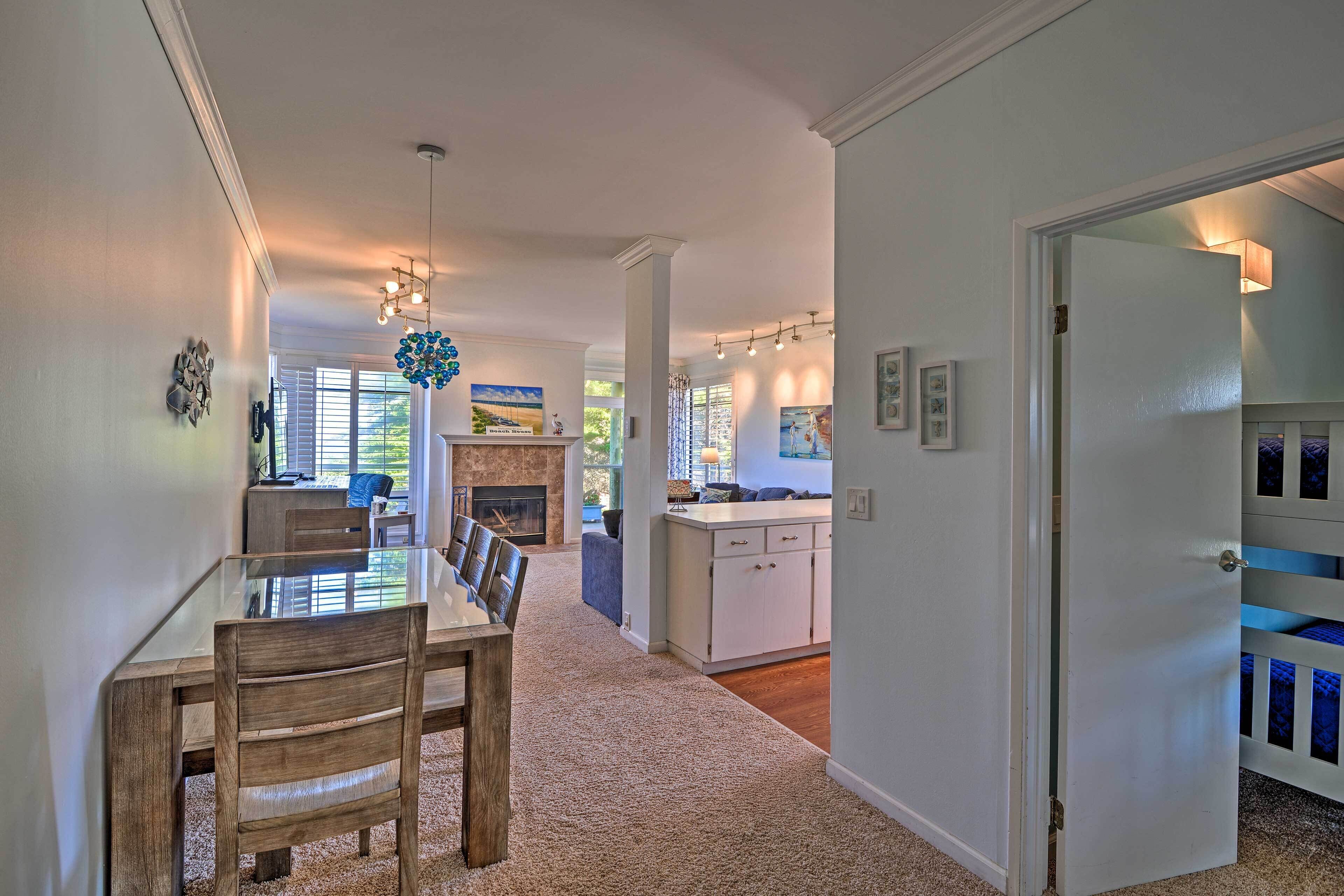 A spacious living area with a dining table, chairs, a fireplace, and a kitchen in the background.