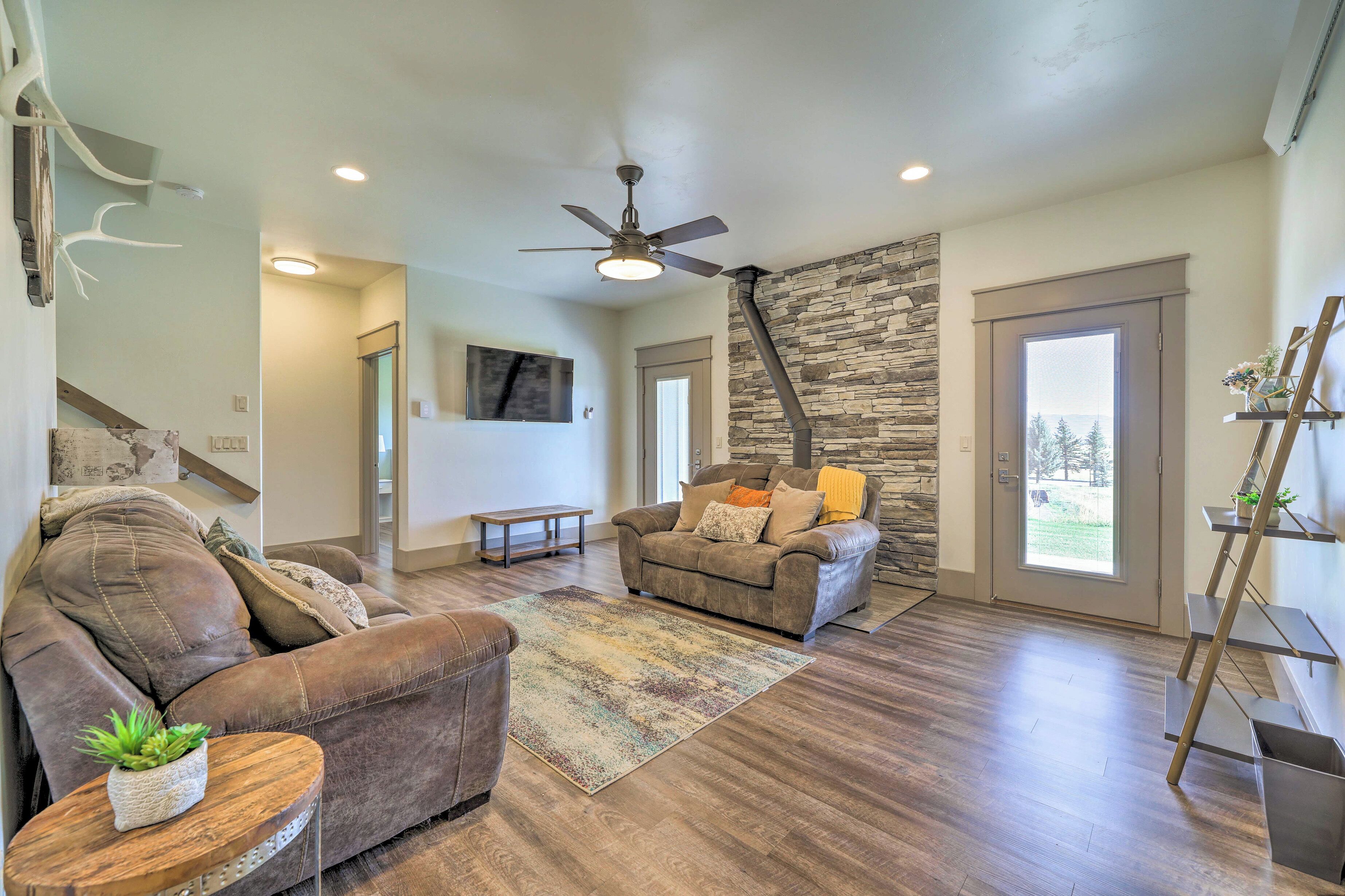 A spacious living room with a brown leather sofa, a wooden coffee table with a plant, a stone accent wall, and a large window.