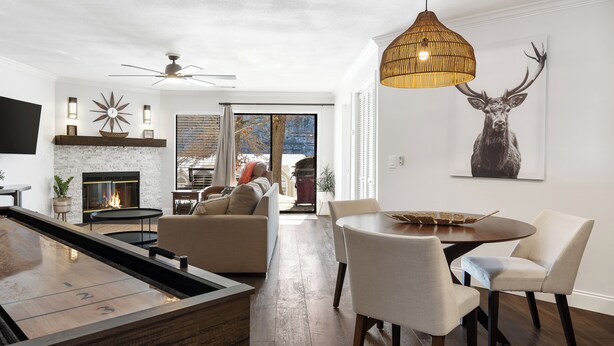 A modern living room with a fireplace, a dining area with a round table and chairs, and a large deer painting on the wall.