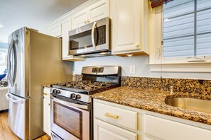 Una cocina con armarios blancos, un refrigerador de acero inoxidable, un microondas, una estufa a gas y una encimera de granito.