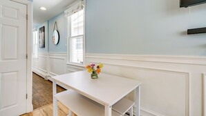Une pièce avec une table blanche, un vase rempli de fleurs, une porte blanche et une fenêtre avec des stores.
