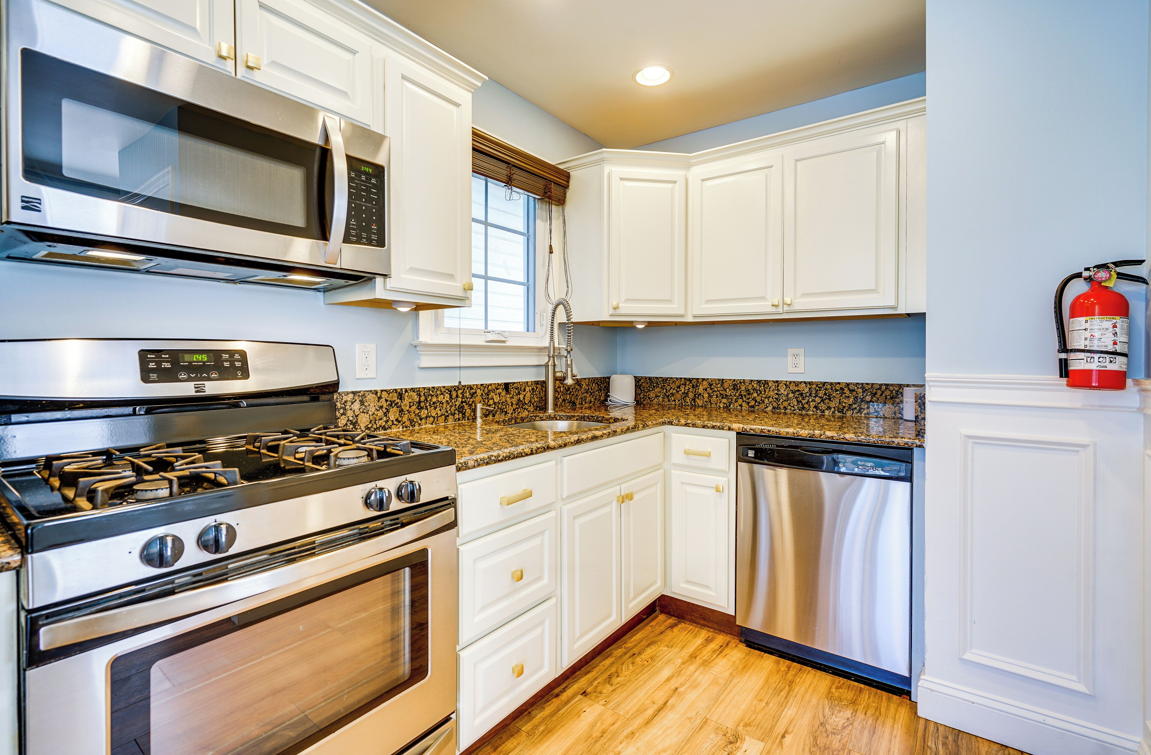 A kitchen with white cabinets, stainless steel appliances, a microwave, stove, sink, and dishwasher.