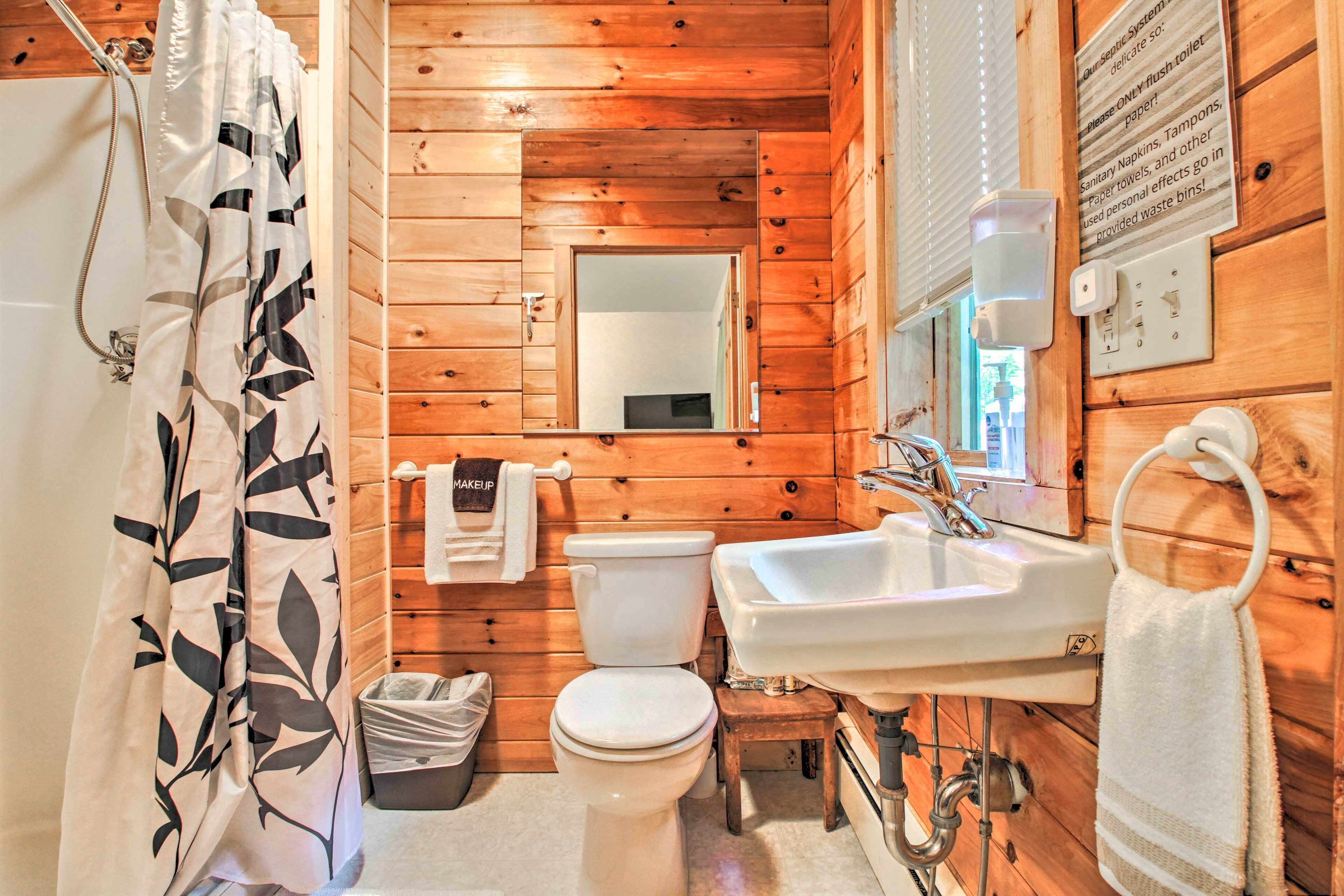 A wooden cabin bathroom with a shower, toilet, sink, and a mirror.