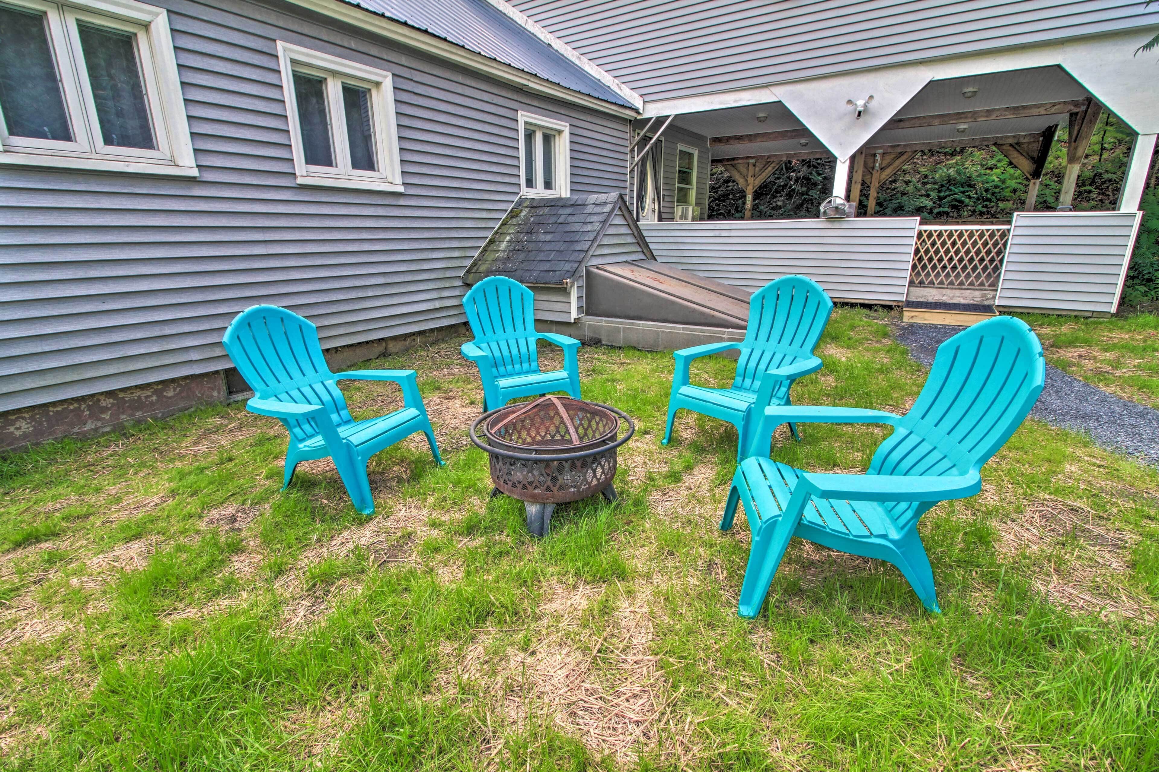 A backyard with four turquoise Adirondack chairs arranged around a central fire pit.