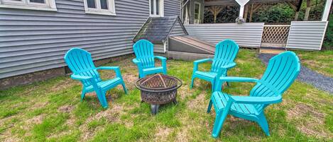 A backyard with four turquoise Adirondack chairs arranged around a central fire pit.