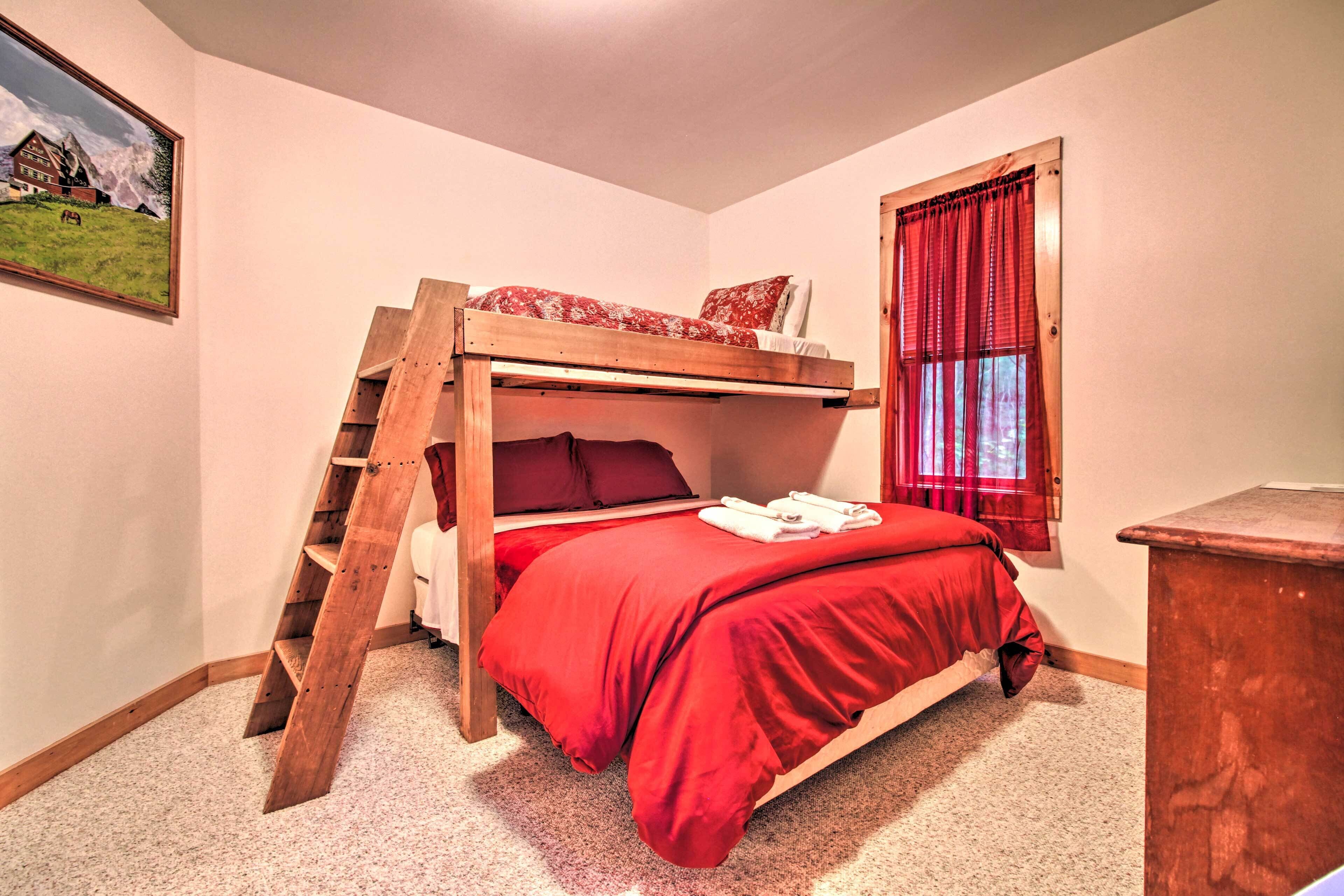 A bunk bed with a wooden ladder, red bedding, a window with red curtains, and a painting on the wall.
