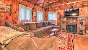 A cozy cabin interior with a wooden interior, a sofa set, a fireplace, and a television mounted above it. - Ludlow Home w/ Hot Tub, Near Okemo Resort! (Ludlow)
