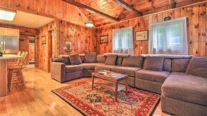 A cozy cabin interior with a wooden ceiling, a living area with a sofa and a coffee table, and a kitchen area with wooden cabinets and a refrigerator. - Ludlow Home w/ Hot Tub, Near Okemo Resort! (Ludlow)