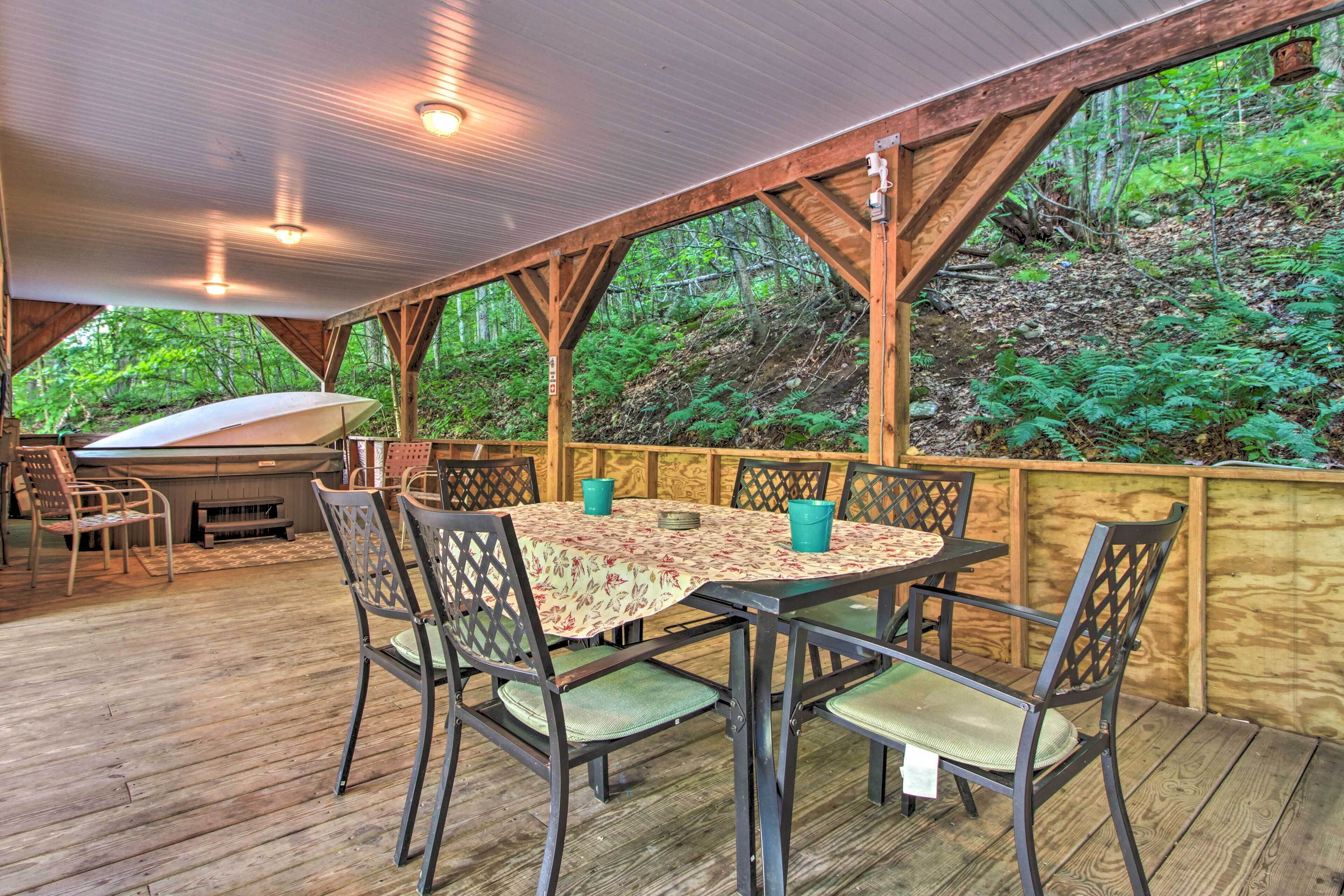Une terrasse extérieure en bois, avec une table ronde et des chaises, entourée d’une clôture en bois, et donnant sur une zone boisée.