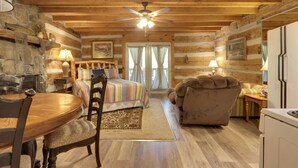A log cabin interior with a wooden dining table, a bed with a striped blanket, a sofa, and a ceiling fan. - 3 Mi to Natl Park: Townsend Apt on Little River! (Townsend)