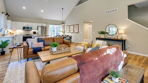 A spacious living area with a sofa, coffee table, and dining table. There is a kitchen in the background with modern appliances. - Chic Wisconsin Retreat w/ Deck, Grill & Fire Pit! (Wisconsin Dells)