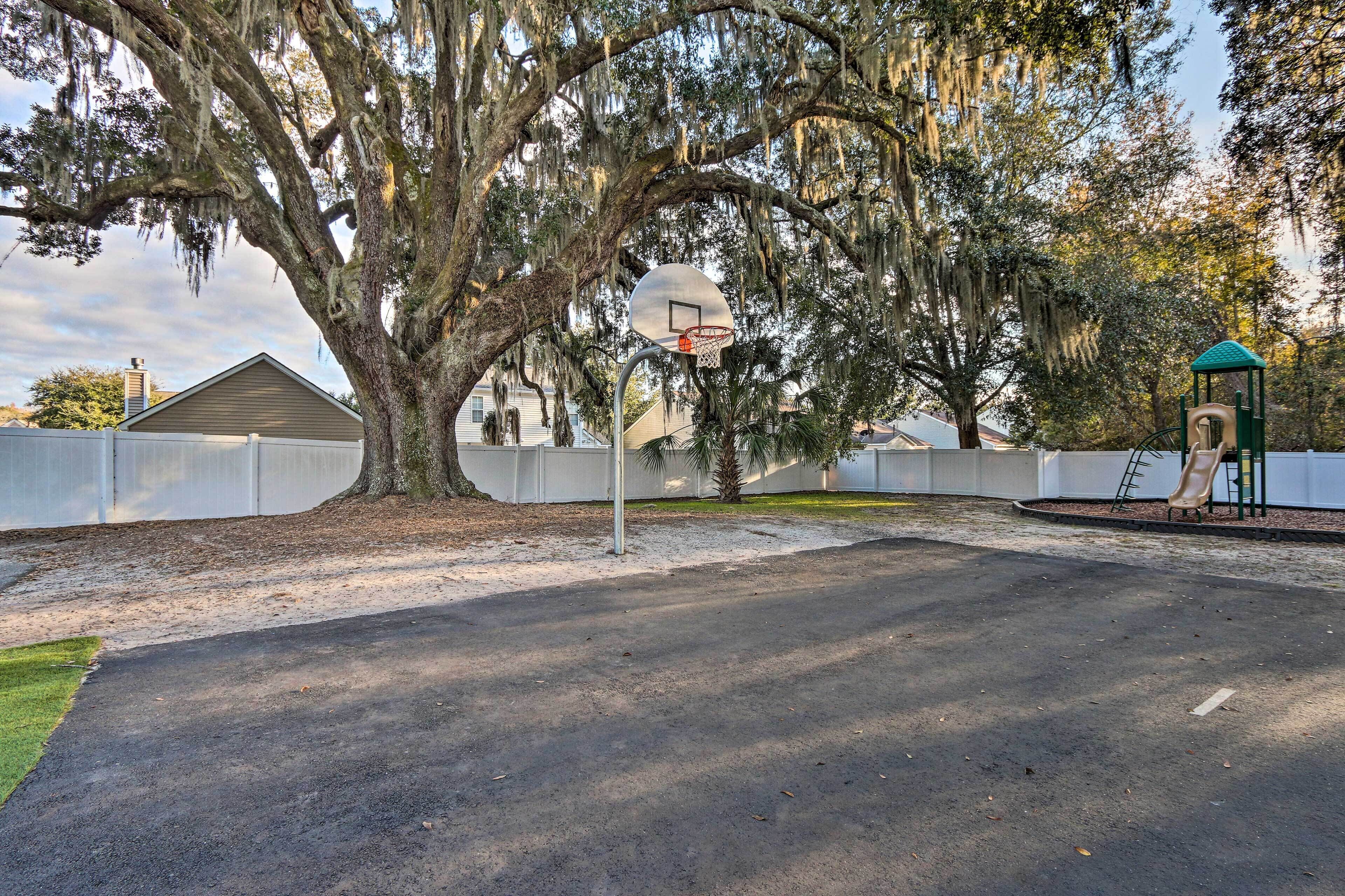 A basketball court with a hoop, surrounded by trees and a playground.