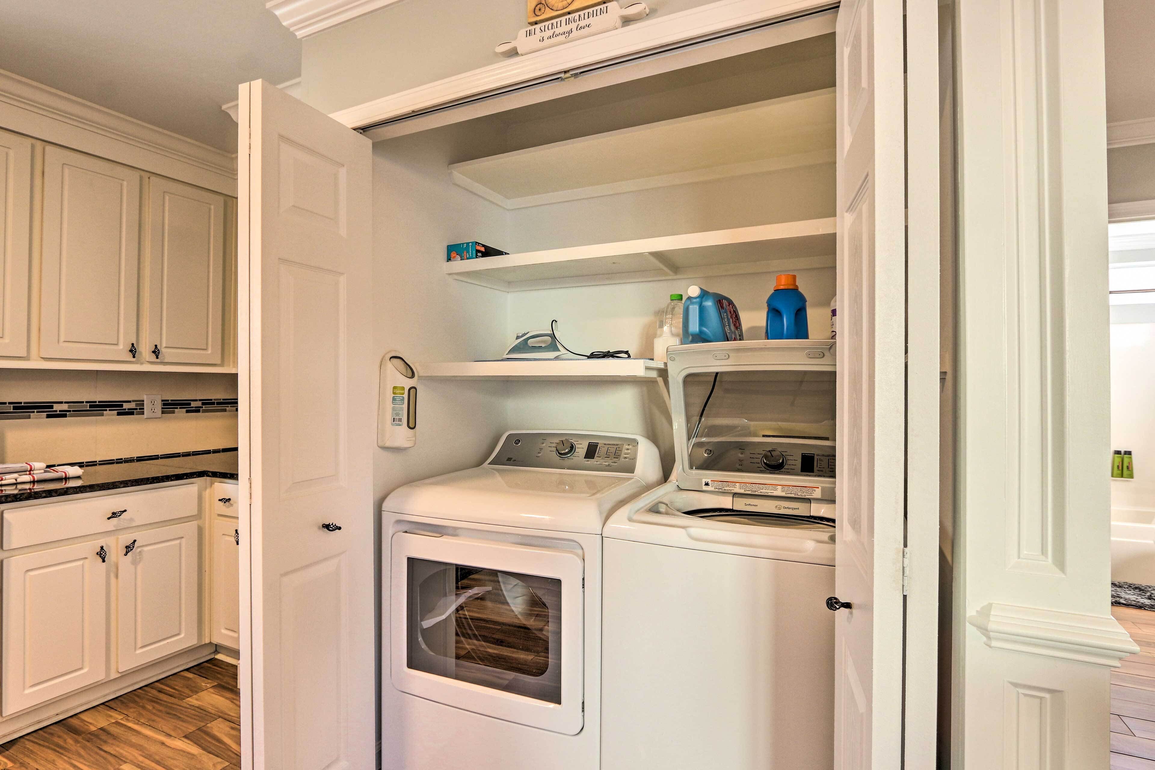 A compact laundry room with a front-loading washer and dryer, a shelf with cleaning supplies, and a microwave above the dryer.