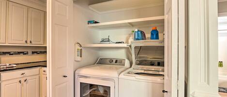 A compact laundry room with a front-loading washer and dryer, a shelf with cleaning supplies, and a microwave above the dryer.