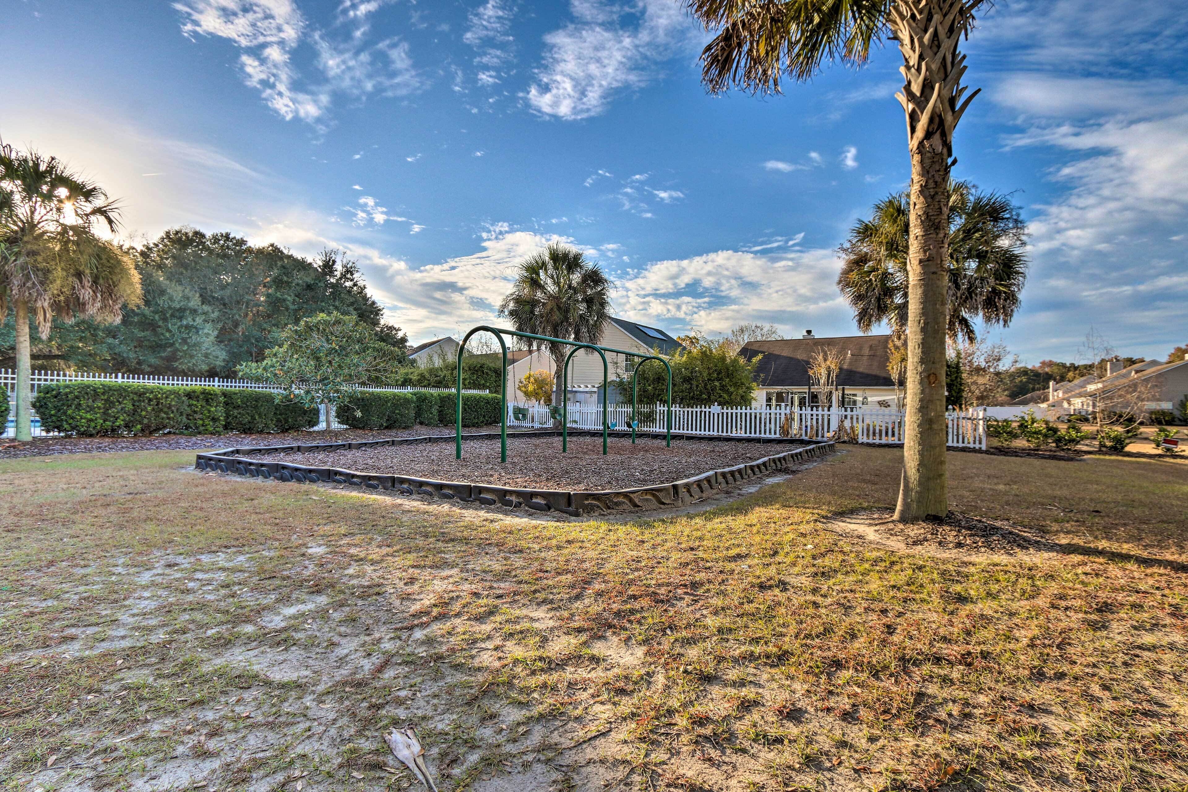 A park with a playground, white picket fence, and palm trees.