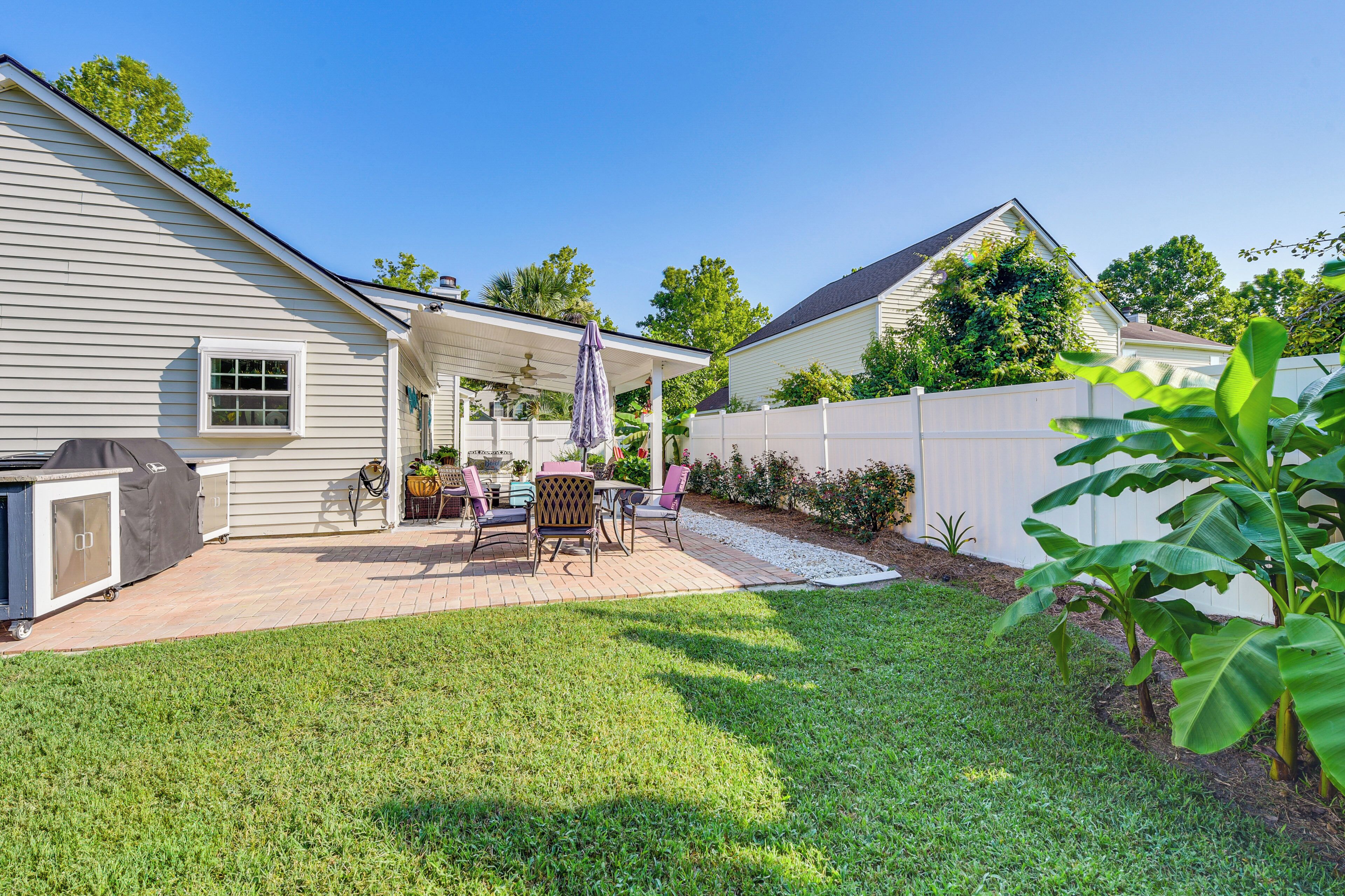 A backyard with a covered patio, a grill, and a fenced area.