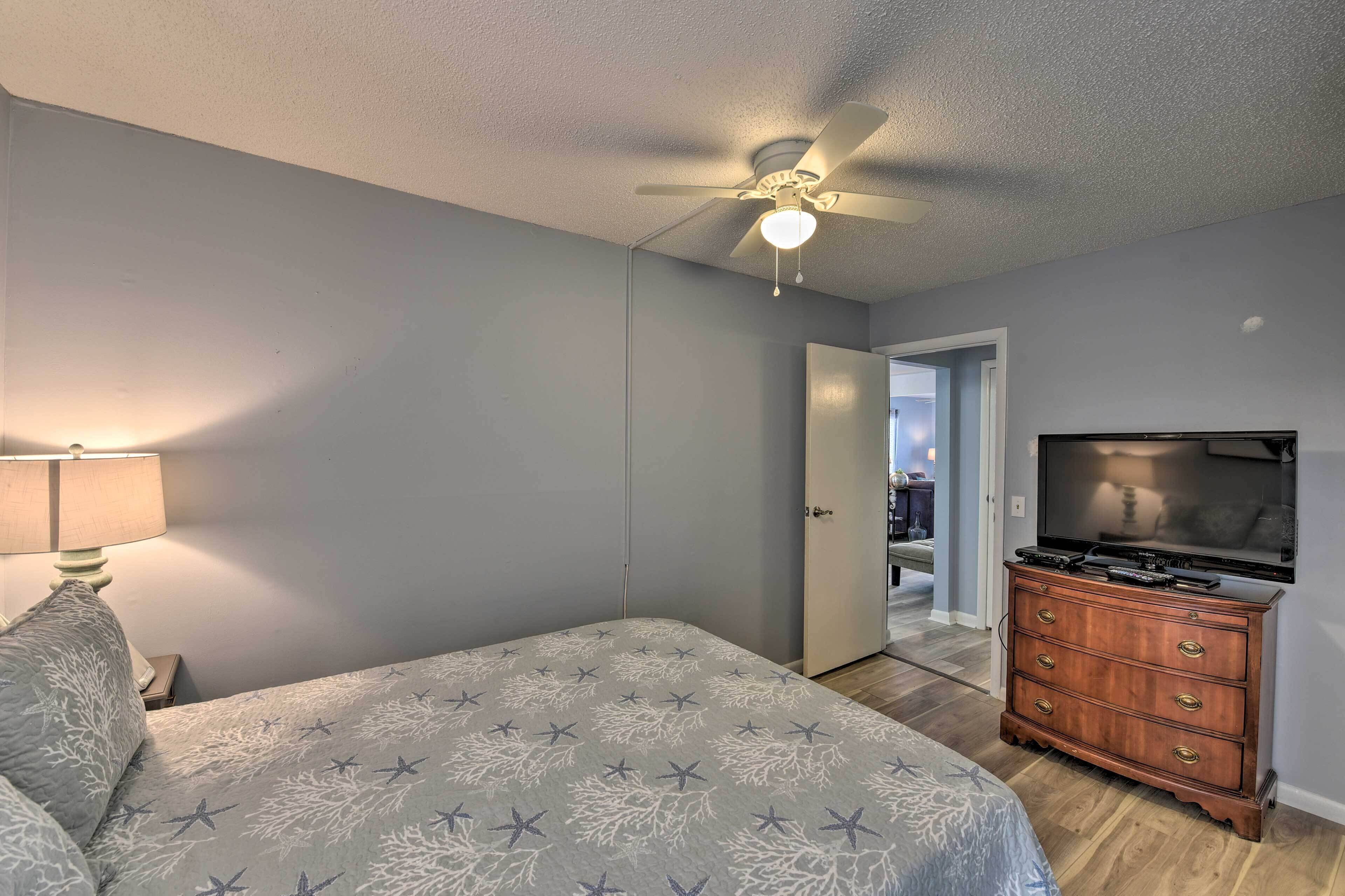 A bedroom with a bed, a dresser, a ceiling fan, and a television.