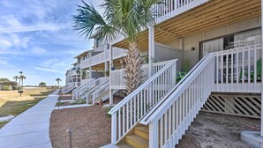 A multi-story residential building with white railings, a palm tree, and a concrete pathway.