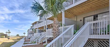 A multi-story residential building with white railings, a palm tree, and a concrete pathway.