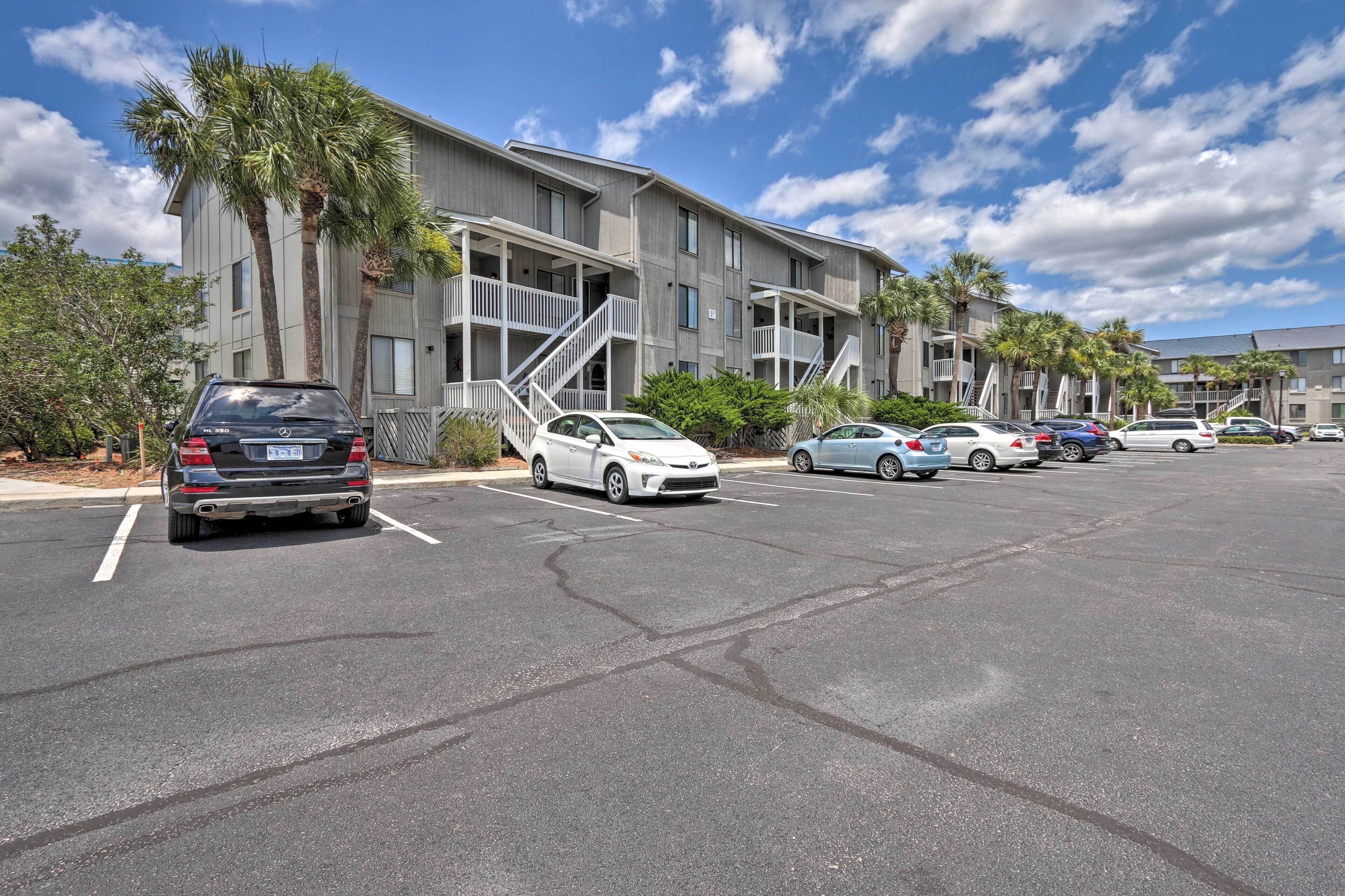 A parking lot with several cars and a building with multiple floors and balconies.