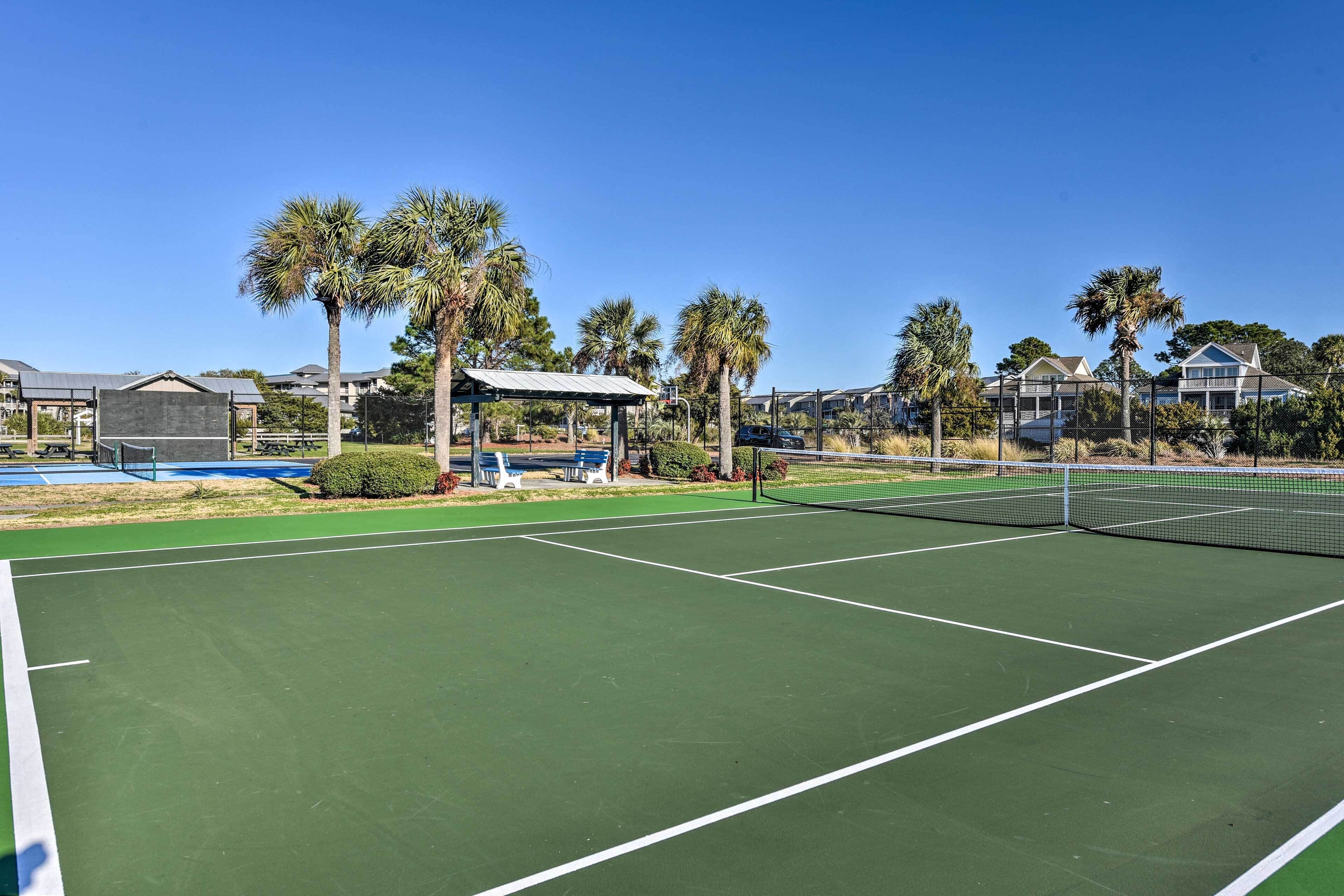 Een tennisbaan met een net, omringd door palmbomen en een overdekt zitgedeelte.