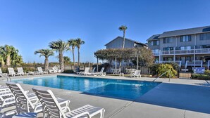 A swimming pool with lounge chairs, palm trees, and a building with balconies.