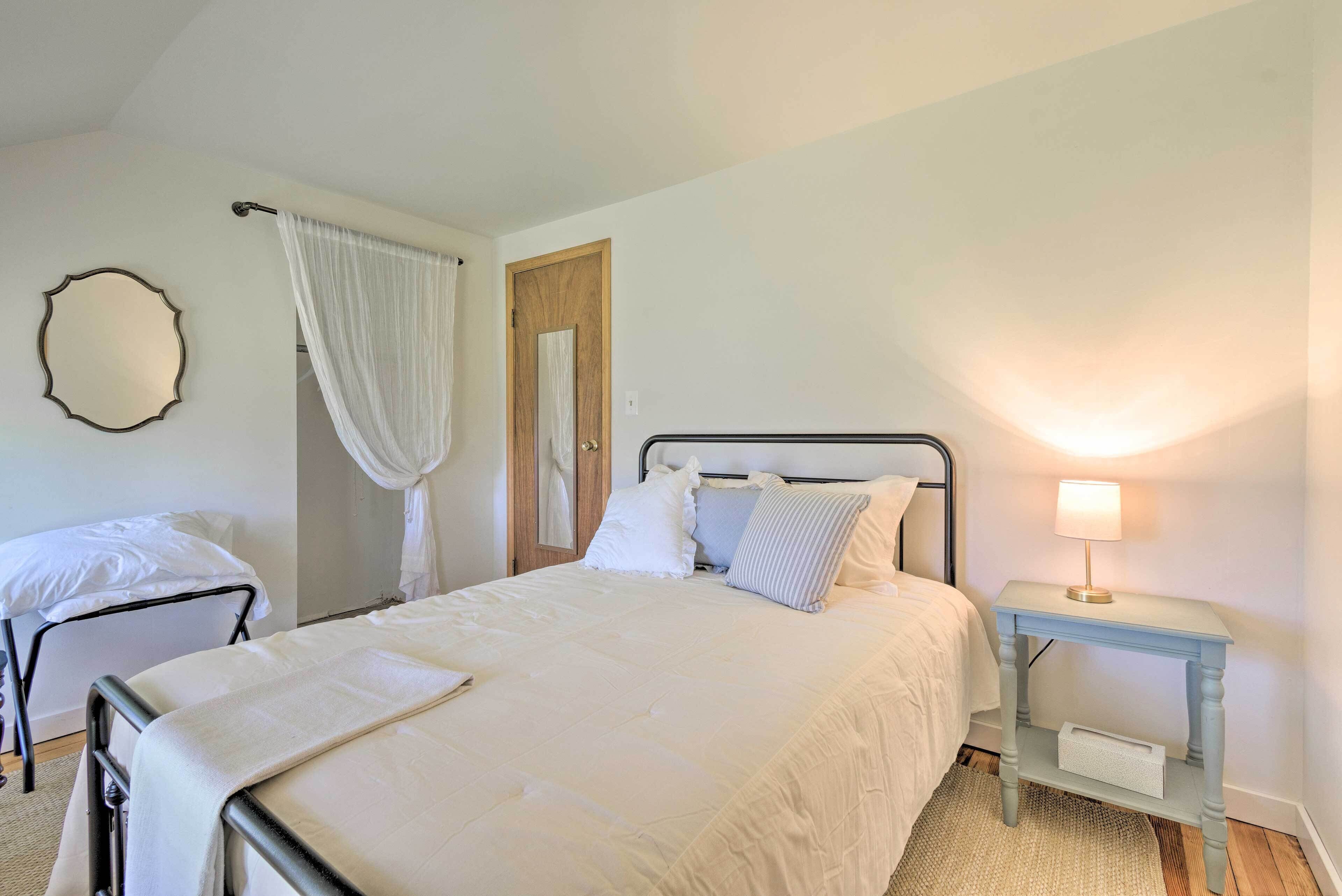 A bedroom with a bed, a bedside table with a lamp, a chair, and a door.