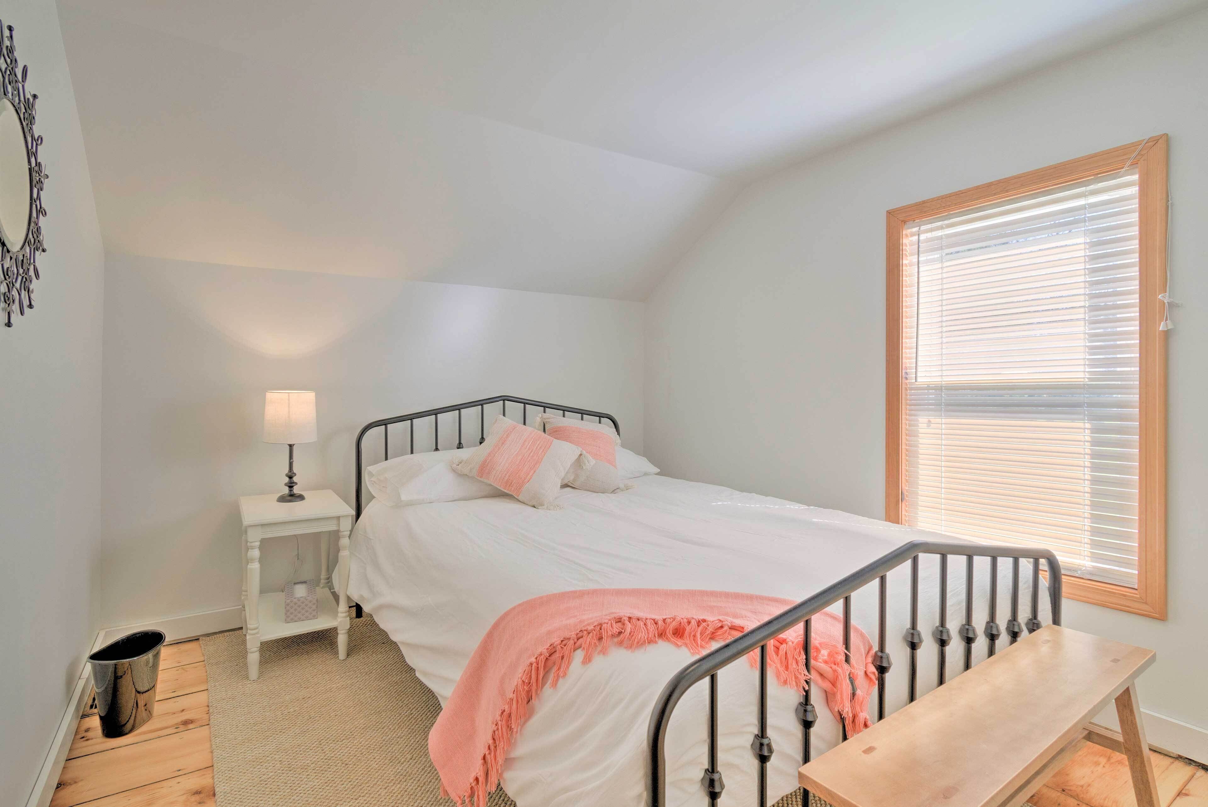 A bedroom with a bed, bedside table, lamp, and a window with blinds.