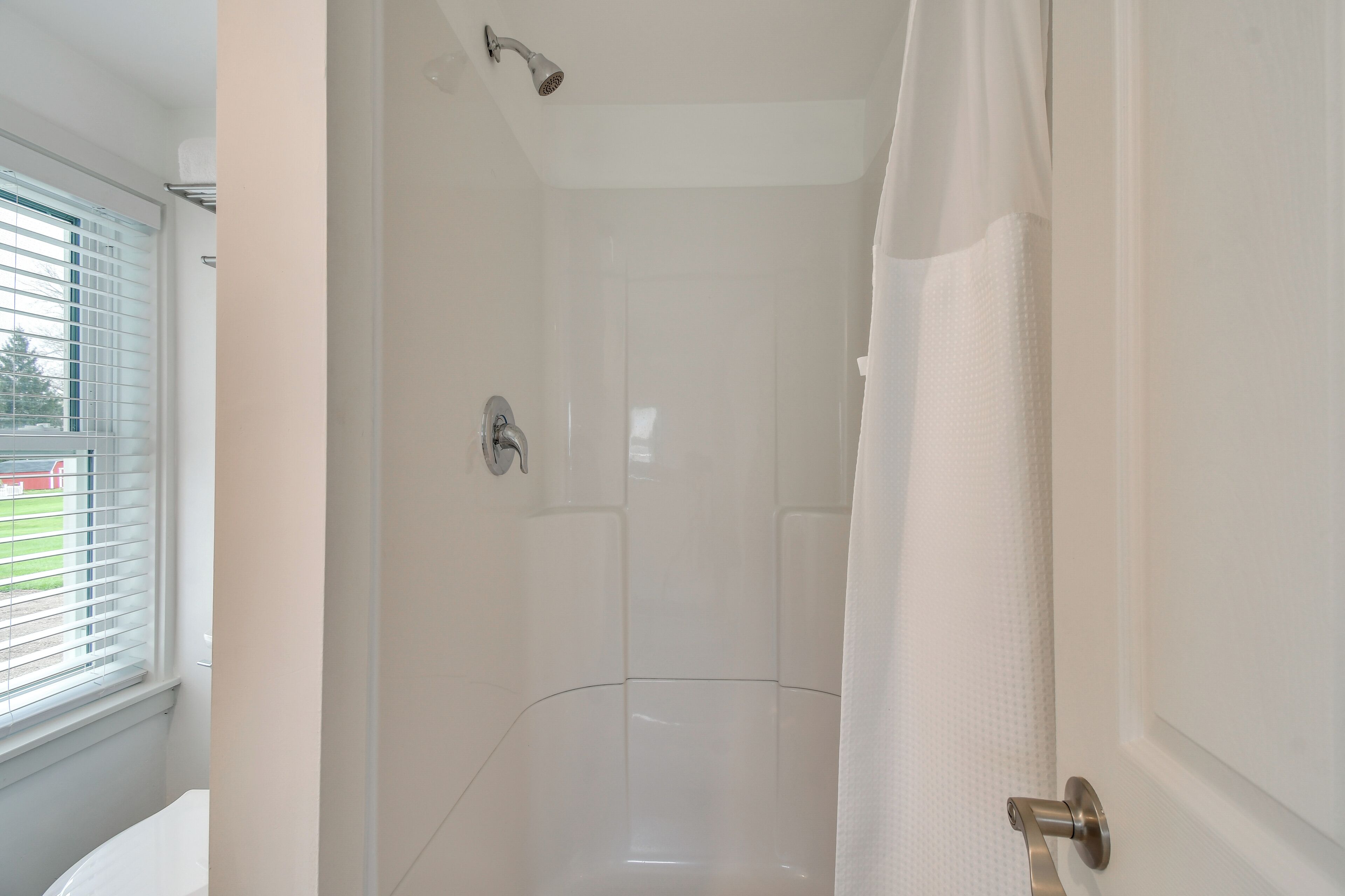 A modern bathroom with a shower, a toilet, and a window with blinds.