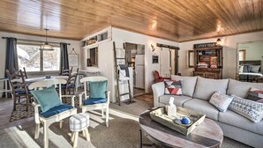 Ein gemütliches Wohnzimmer mit Holzboden, einer Couch, Sesseln, einem Couchtisch und einer sichtbaren Küchenzeile im Hintergrund.