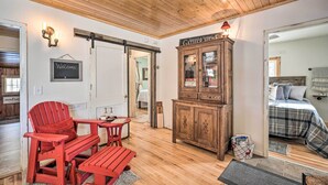 Ein gemütliches Zimmer mit Holzbalkendecke, einem roten Adirondack-Sessel, einem kleinen Tisch, einem Schrank und einem Bett mit karierter Decke.