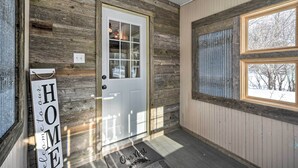 Ein Holzgebäude mit einer weißen Tür, einem Willkommensschild und einem Fenster mit Blick auf Bäume.